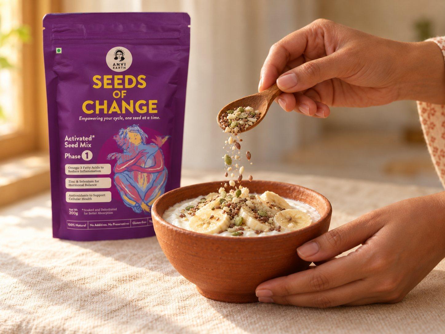 A hand sprinkling a spoonful of activated seed mix over a bowl of yoghurt, the Seeds of Change pack behind